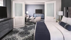 Une chambre d’hôtel avec un grand lit, une télévision, un bureau avec une chaise et une petite table avec une lampe.