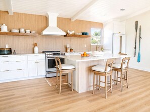 A modern kitchen with white cabinetry, a central island with bar stools, and a large stove. - Newly Renovated! Gulf Views! DRIFT on Indian Pass (Port St. Joe)