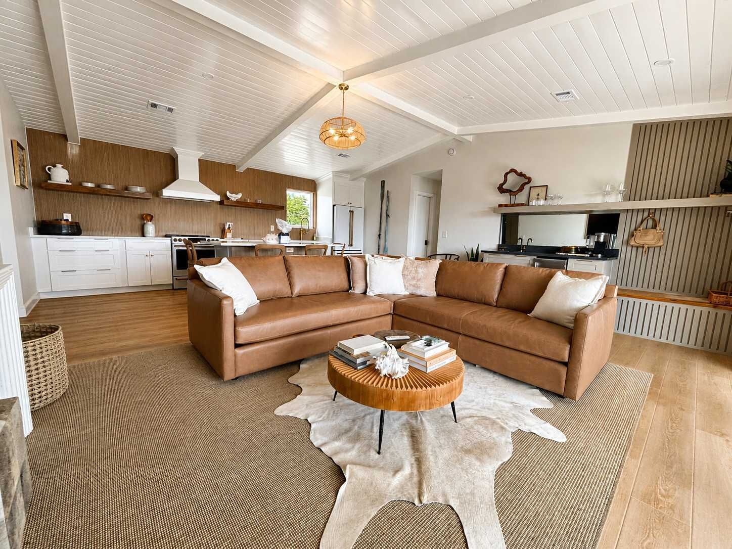 Ein modernes Wohnzimmer mit einem braunen Ledersofa, einem runden Couchtisch aus Holz und einem Cowhide-Teppich.