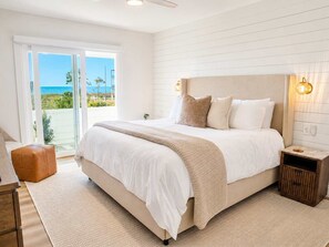 A bedroom with a large bed, a nightstand, a wooden bench, and a view of the outdoors. - Newly Renovated! Gulf Views! DRIFT on Indian Pass (Port St. Joe)