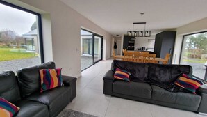 Ein modernes Wohnzimmer mit einer schwarzen Ledersofa, einem Esstisch mit Stühlen und einer Küche im Hintergrund.