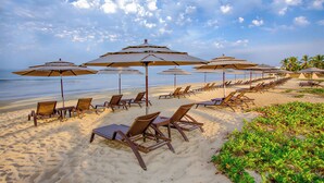 Ein Strand mit Liegestühlen und Sonnenschirmen, einem klaren Himmel und Palmen im Hintergrund.