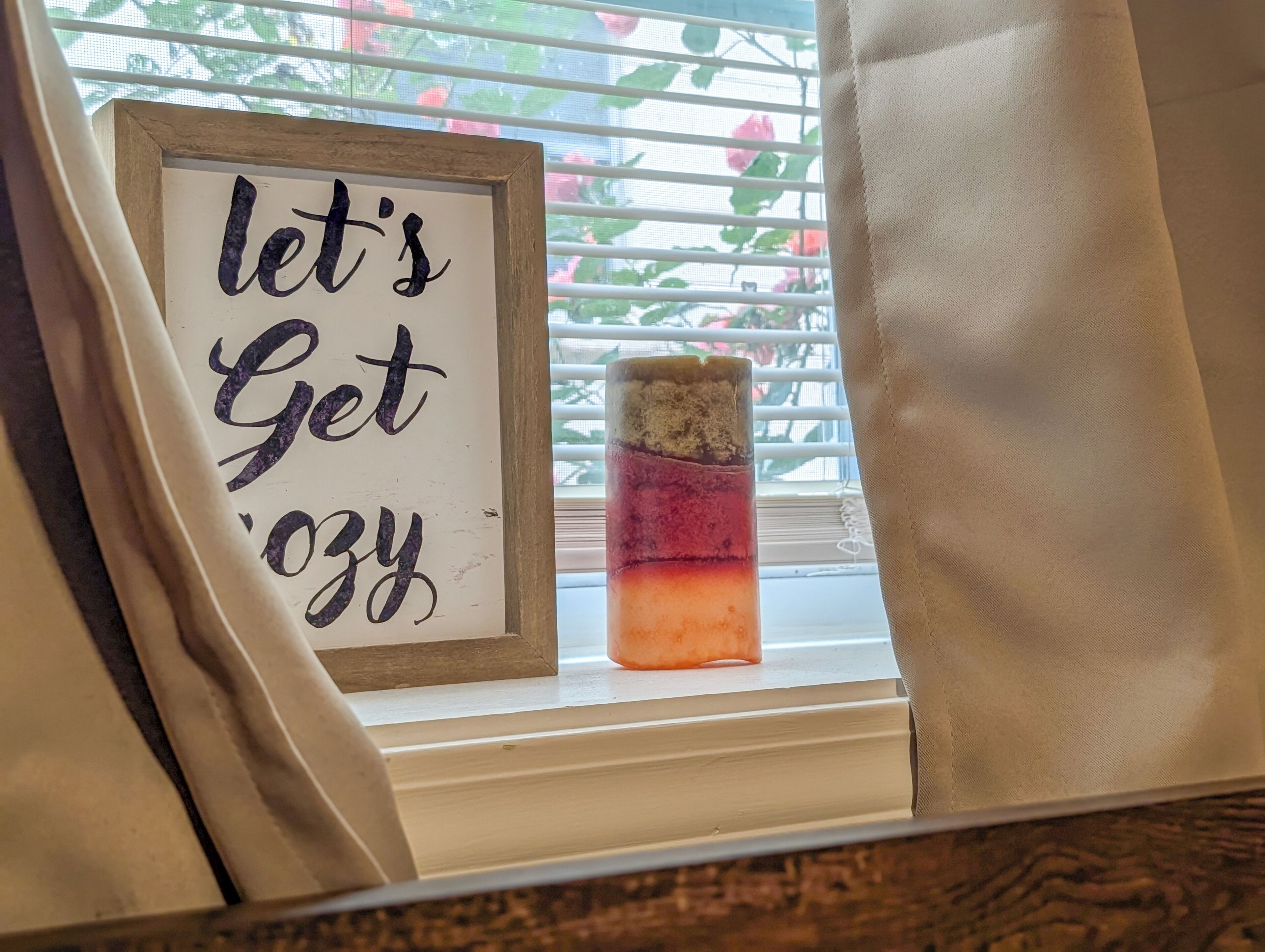 A framed sign with the text 'let's Get 'Ozy' and a candle in a glass jar on a windowsill.