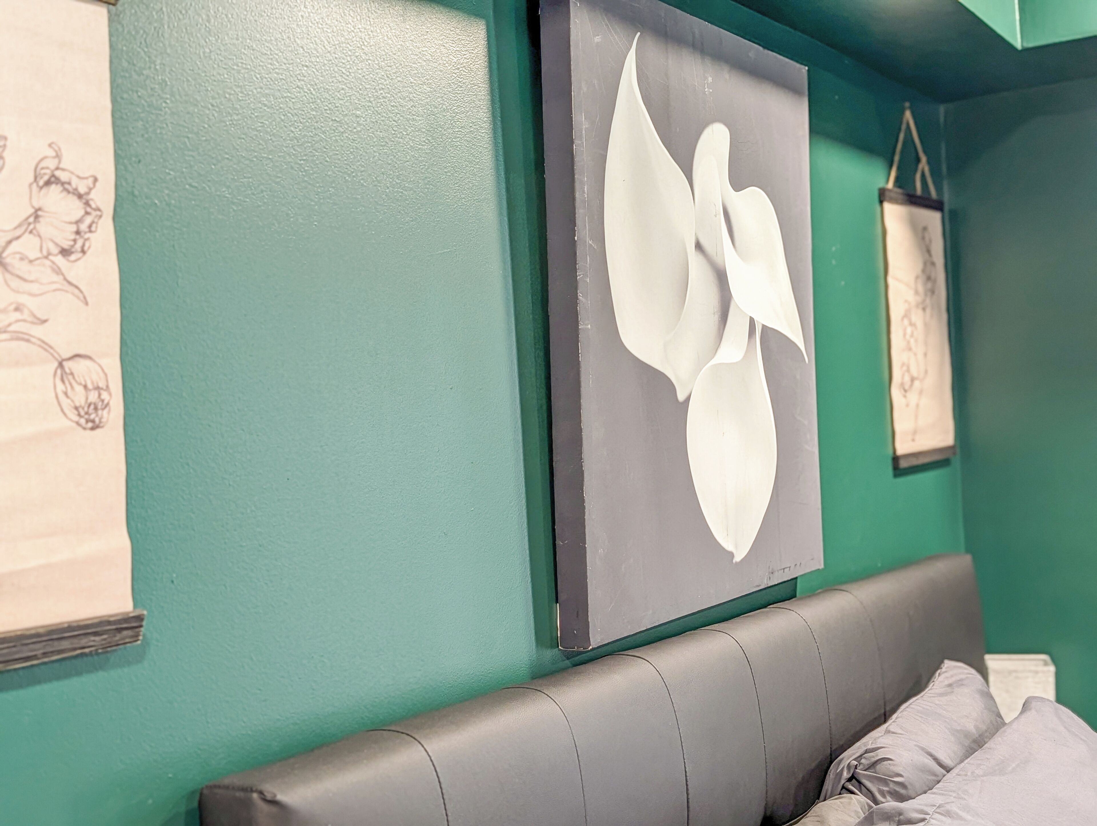 A room with teal walls, a grey leather headboard, and a white abstract painting.