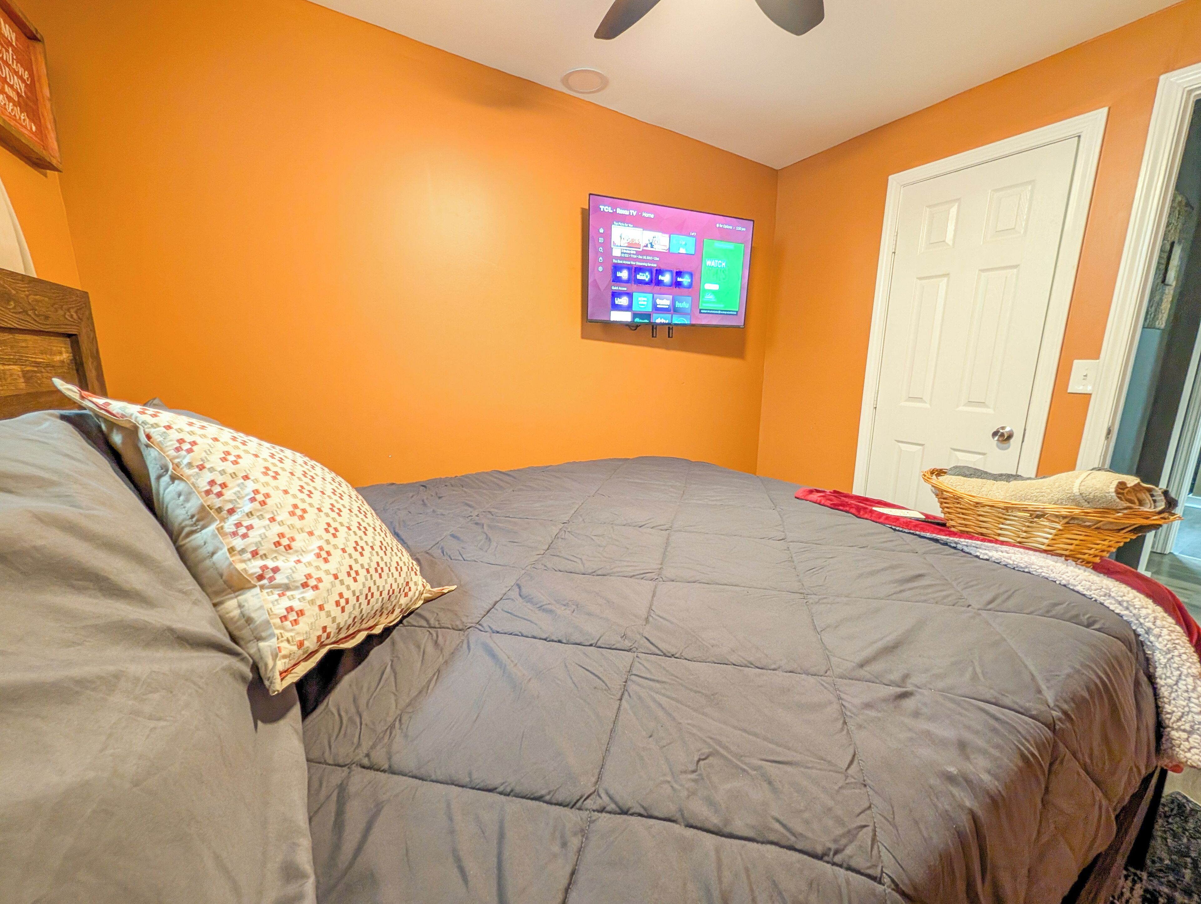 Un dormitorio con cama, televisión montada en la pared y una puerta.