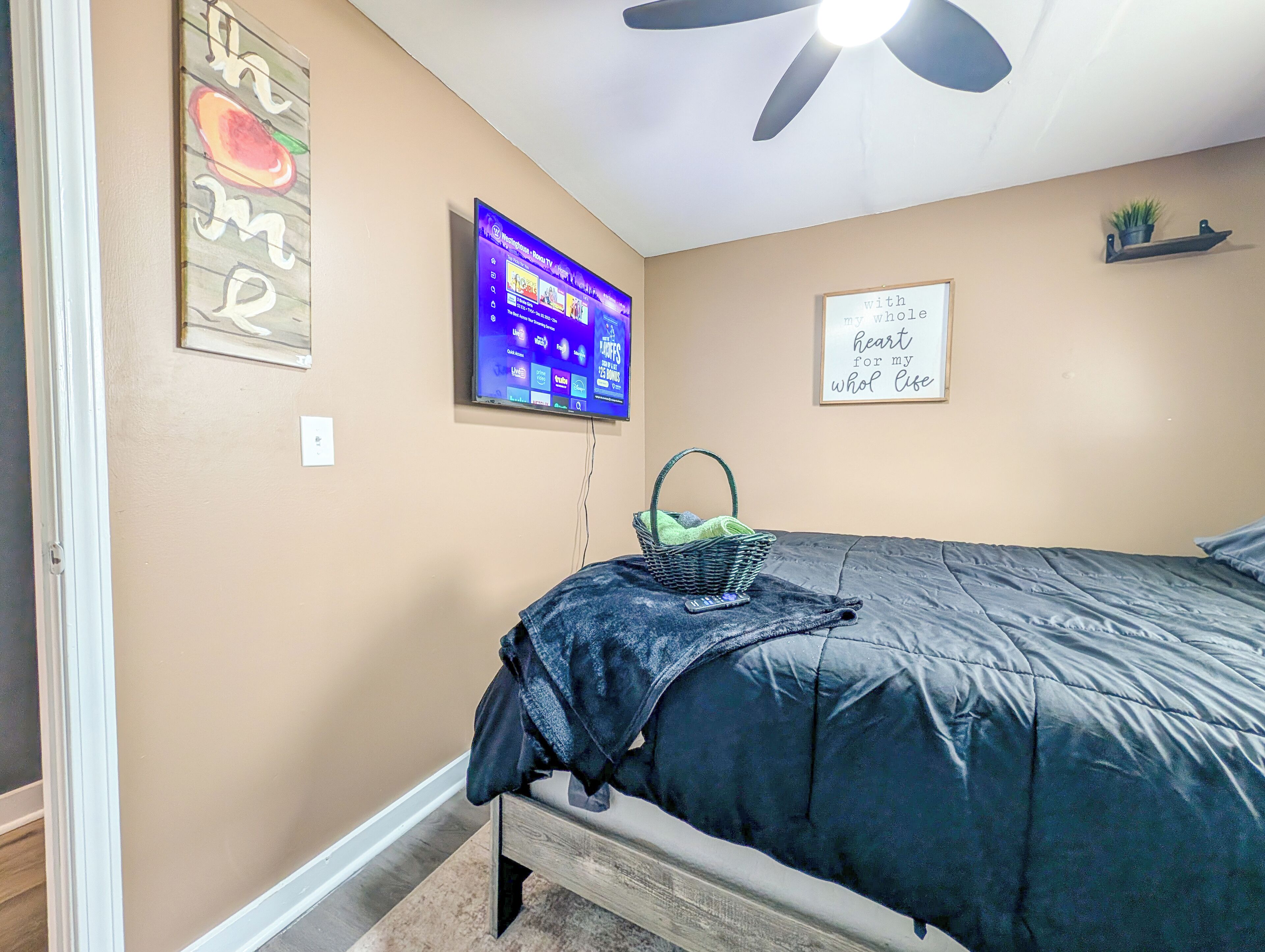 Un dormitorio con cama, ventilador de techo, televisión montada en la pared y una cita motivacional.