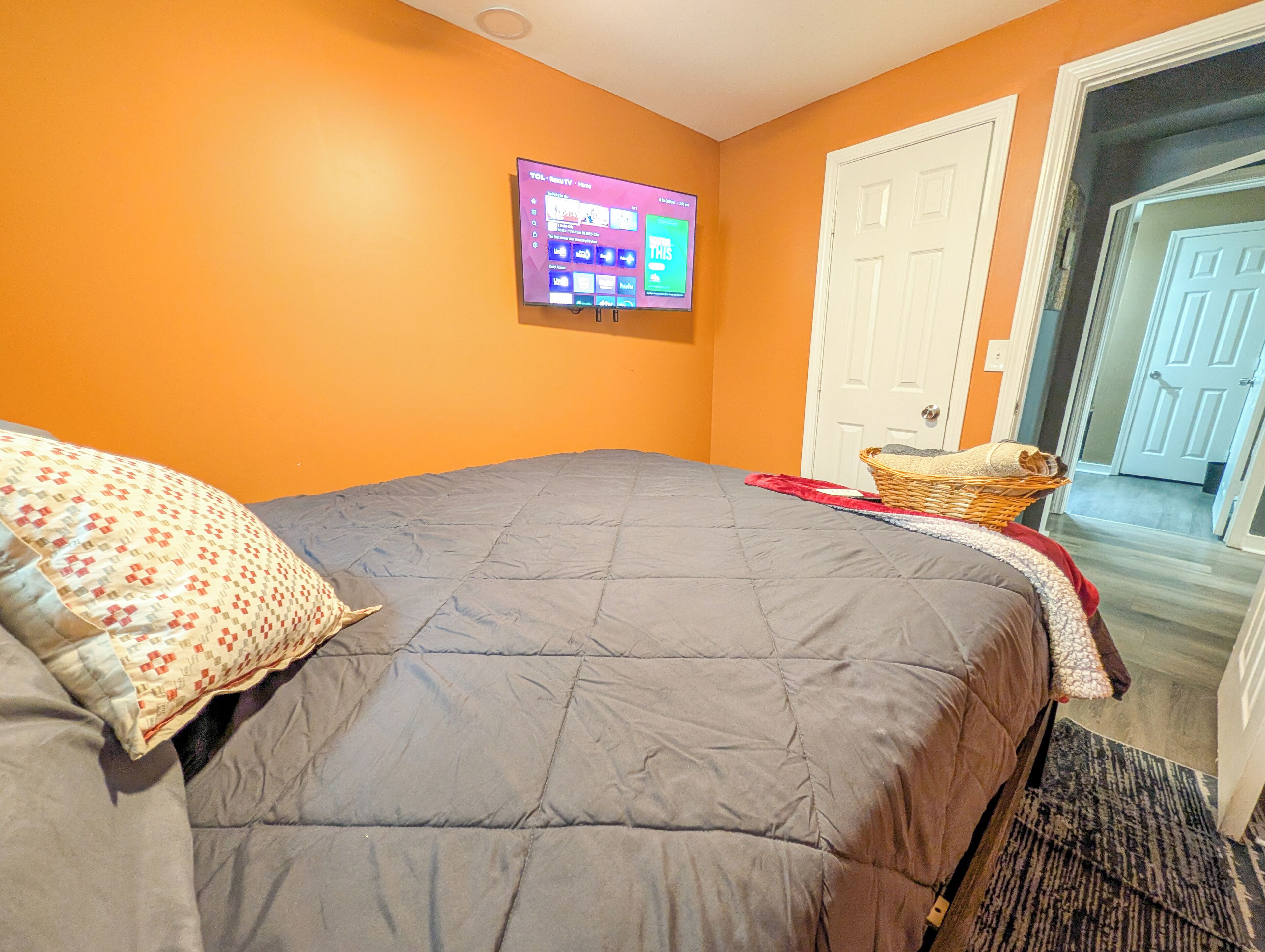A bedroom with a bed, a television mounted on the wall, and a door leading to another room.