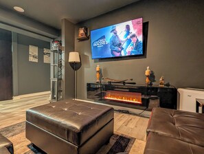 Una sala de estar con televisor de pantalla plana, reposapiés de cuero, chimenea y estantería.