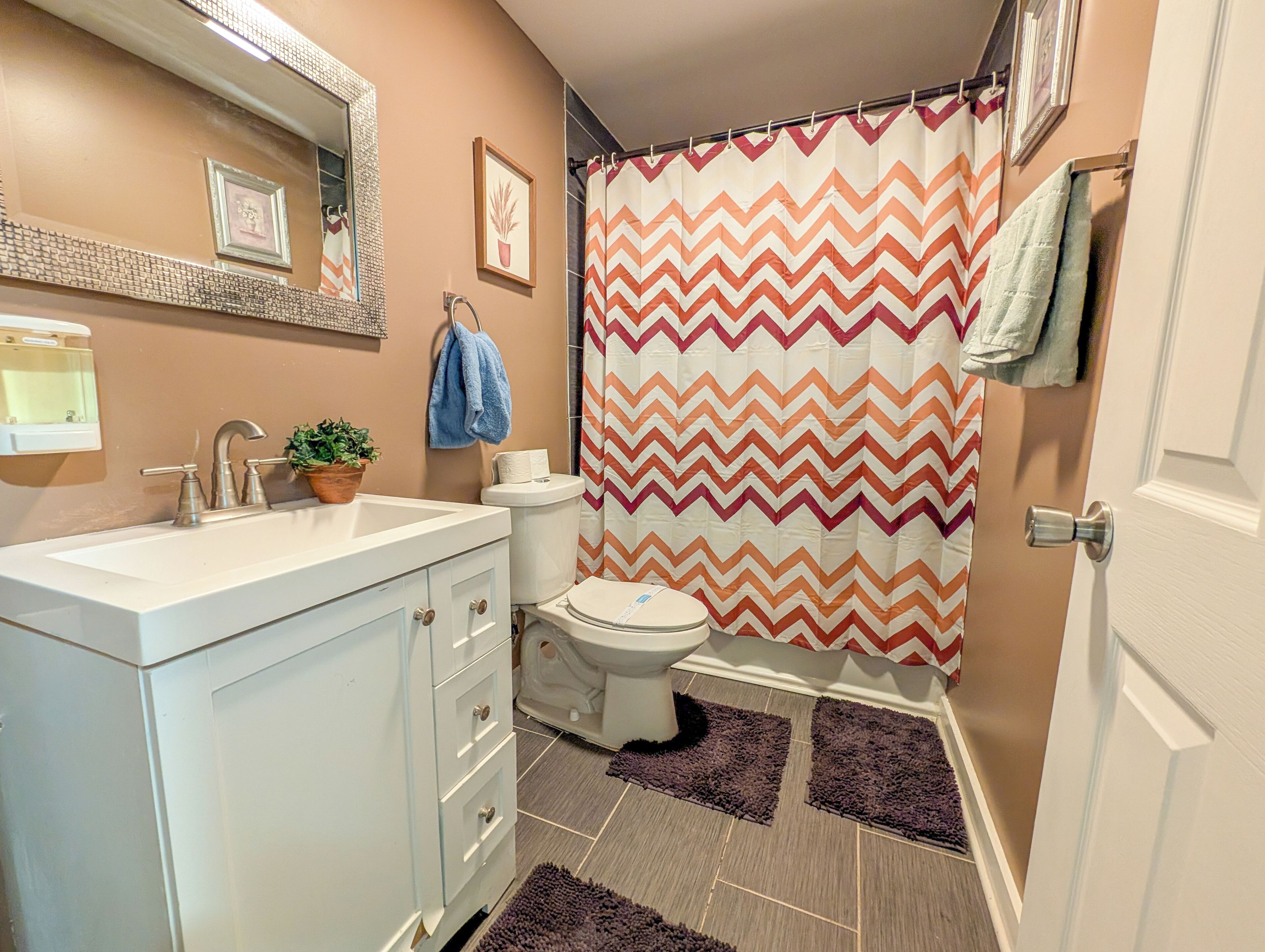 A bathroom with a white sink, a toilet, a shower curtain with a zigzag pattern, a blue towel, and a potted plant.