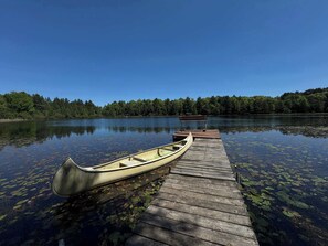 A wooden dock extending into a calm lake with a canoe docked at the end.