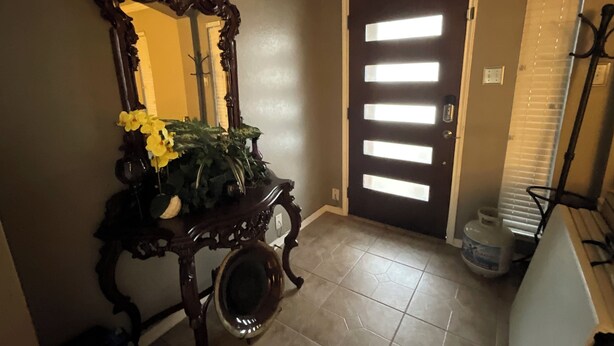 A hallway with a dark brown door, a wooden console table with a mirror and yellow flowers, and a tiled floor. - Spacious 4-bedroom house with AC in fantastic Houston neighborhood (Houston)
