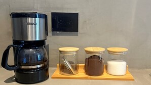 A coffee maker labeled 'imusa' on a wooden tray with three glass containers and a black electrical outlet on the wall. - Loft Private (Cartagena)