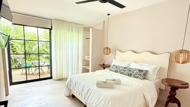 A bedroom with a large bed, a ceiling fan, a view through a sliding glass door, and a small table with a lamp. - Loft Private (Cartagena)