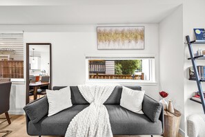 A modern living room with a grey sofa, white throw blanket, and a view of a balcony. - Modern Seattle Home w/ Rooftop Views | Near UW (Seattle)