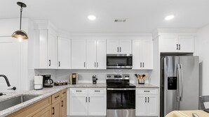 A modern kitchen with white cabinets, stainless steel appliances, a granite countertop, and a wooden floor. - MusicCityRetreat|3BR2BA|Arcade|Sleep8|EasyDTCommute (Madison)