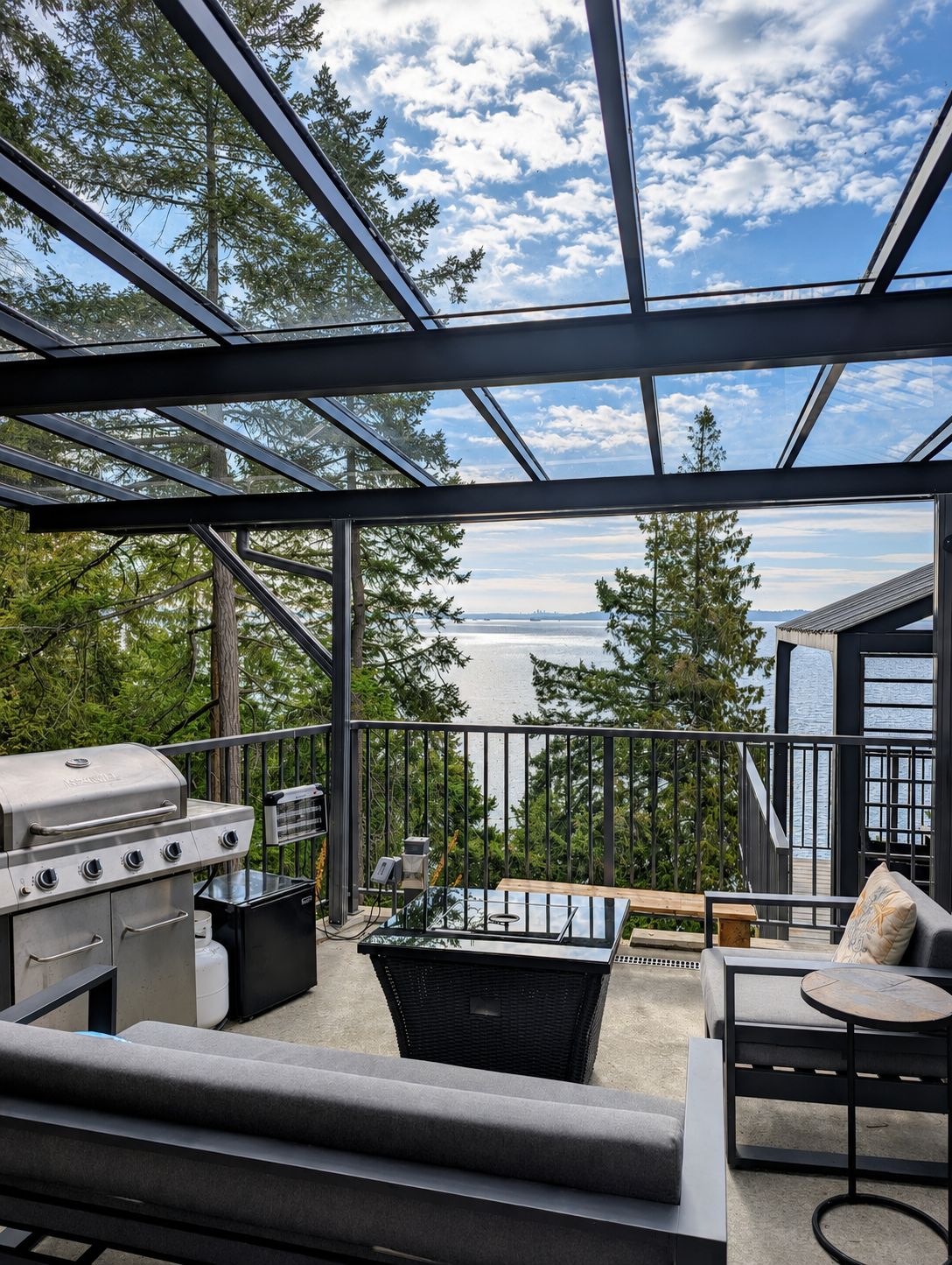 Une terrasse extérieure moderne, équipée d’un barbecue, de sièges et offrant une vue sur l’eau.