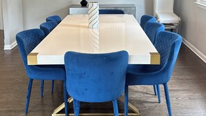 Un coin repas avec une table rectangulaire, des chaises à revêtement bleu, un lustre et une œuvre d’art encadrée accrochée au mur.