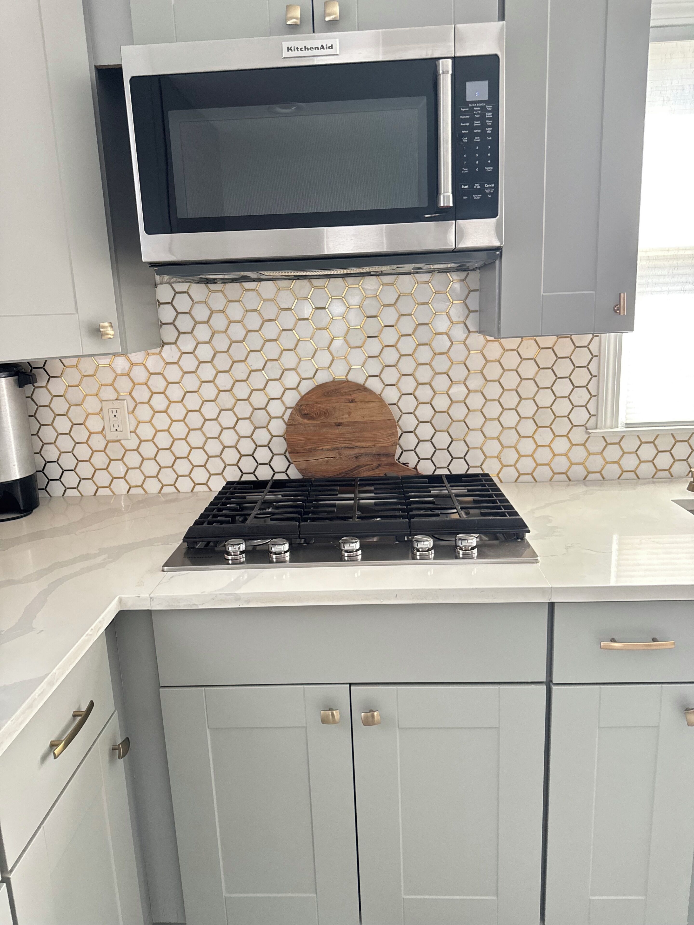 A kitchen with a KitchenAid microwave, a gas stove, and a hexagonal tile backsplash.