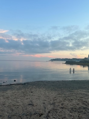 Una playa con mar tranquilo, orilla arenosa y una costa distante con edificios.