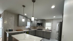 Une cuisine moderne dotée d’un îlot central, de meubles gris, d’un réfrigérateur en acier inoxydable et d’un four à micro-ondes.