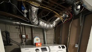Une buanderie équipée de deux machines à laver Samsung, d’un distributeur de lessive Tide, et dont la plomberie et le câblage électrique sont apparents.