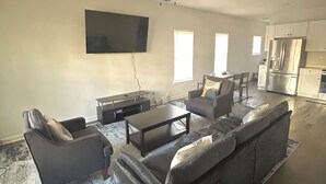 Ein modernes Wohnzimmer mit einem Ecksofa, einem Couchtisch und einem an der Wand montierten Fernseher.