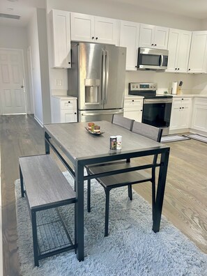 A modern kitchen with white cabinets, stainless steel appliances, and a wooden dining table with benches. - Spacious Atlanta retreat with dimmable lighting (Atlanta)