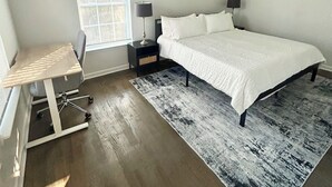 Ein Schlafzimmer mit Bett, Schreibtisch, Stuhl, Nachttisch, Lampe, Fenster und Deckenleuchte.