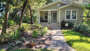 Eenlaags huis met een overdekte veranda, een voordeur en een kleine tuin met diverse planten en een metselpad naar de ingang.