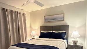 Een hotelkamer met een bed, een plafondventilator, een nachtkastje met lamp en een schilderij aan de muur.
