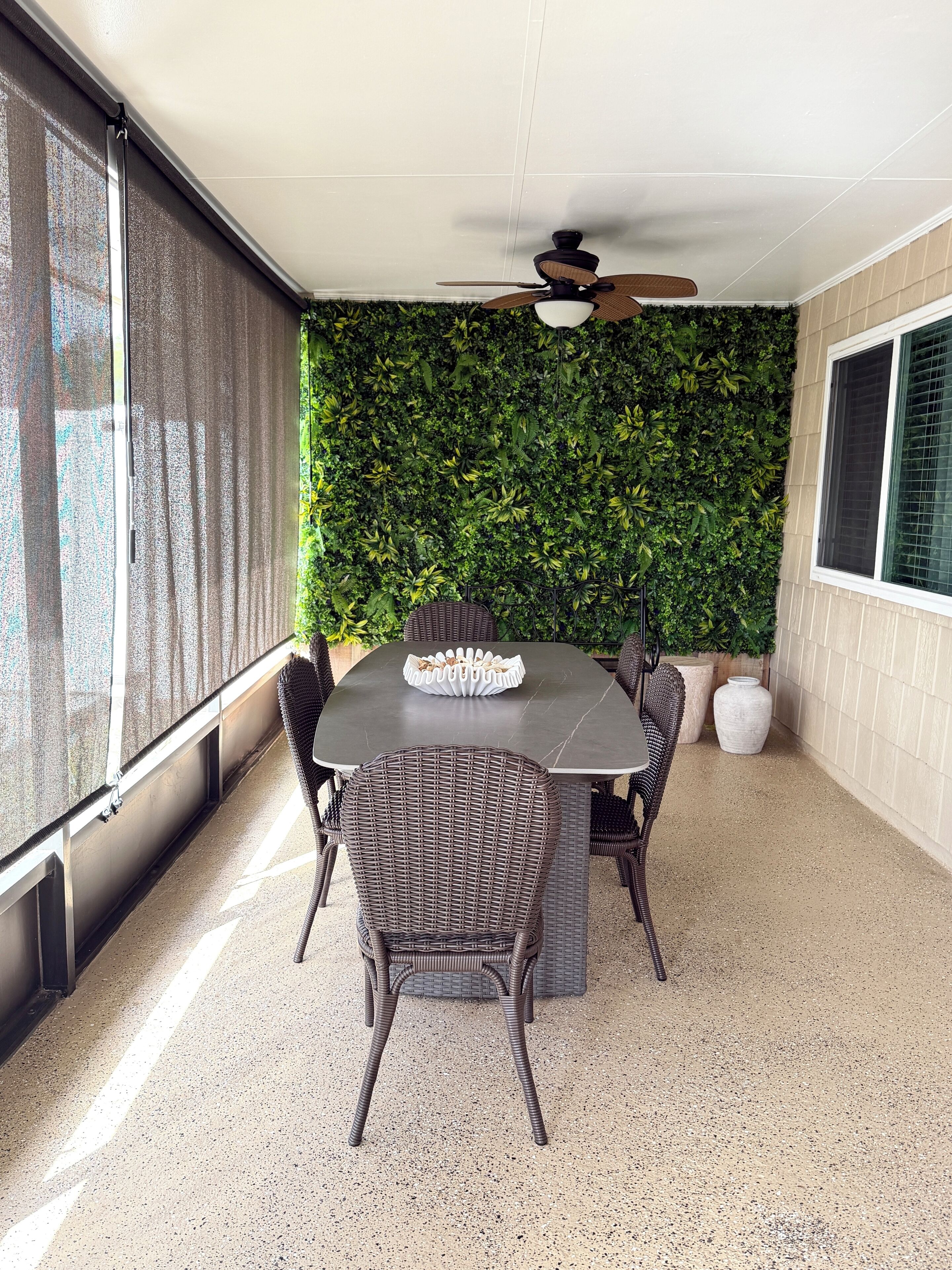 Eine Terrasse im Freien mit Tisch und Stühlen, einem Deckenventilator und einer grünen Wand.