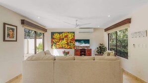 Ein Wohnzimmer mit einem beigefarbenen Ecksofa, einem Deckenventilator, einem Fernseher und Kunstwerken an den Wänden.