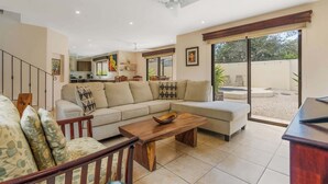 Ein geräumiges Wohnzimmer mit einer großen Couch, einem Holztisch und einem Essbereich. Im Hintergrund ist eine Küche zu sehen, und eine Glastür führt auf eine Terrasse.
