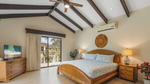 Ein Schlafzimmer mit einem hölzernen Bett, einem Deckenventilator, einem Fernseher und Blick ins Freie.