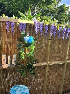 Ein Bambuszaun mit hängenden violetten Blüten und einem Regal mit Pflegeprodukten.