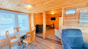 A cozy cabin interior with a dining area, a blue armchair, and a sign reading "Lake House" with various activities listed. - Wiggin Stream Camp five-minute`s to public beach and boat launch! (Greenville)