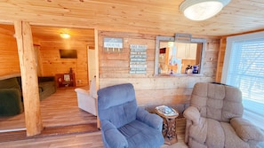 A cozy cabin interior with wooden walls and floors, two plush armchairs, a small table with a book, and a sign listing 'Lake House' and 'Moose Crossing'. - Wiggin Stream Camp five-minute`s to public beach and boat launch! (Greenville)