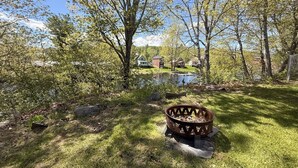 A backyard with a fire pit, a pond, and a house in the background. - Wiggin Stream Camp five-minute`s to public beach and boat launch! (Greenville)