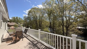 A deck with a table and chairs, a white railing, and trees in the background. - Wiggin Stream Camp five-minute`s to public beach and boat launch! (Greenville)
