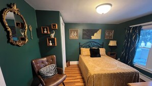 Ein Schlafzimmer mit Bett, Sessel, Kommode, Spiegel und Bildern an den Wänden.
