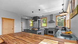 Une cuisine moderne dotée d’un grand îlot central en bois, d’appareils électroménagers en acier inoxydable et de luminaires suspendus.