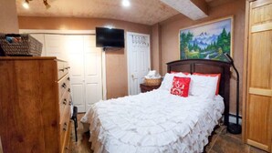 A bedroom with a large bed, a wooden dresser, a television on the wall, and a painting on the wall.