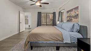 Ein Schlafzimmer mit einem Bett, einem Deckenventilator, einem Gemälde und einer Tür zu einem anderen Raum.