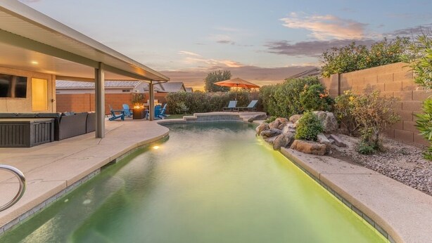 Ein Swimmingpool mit  überdachter Terrasse, Liegestühlen und einer Backsteinmauer mit Bepflanzung.