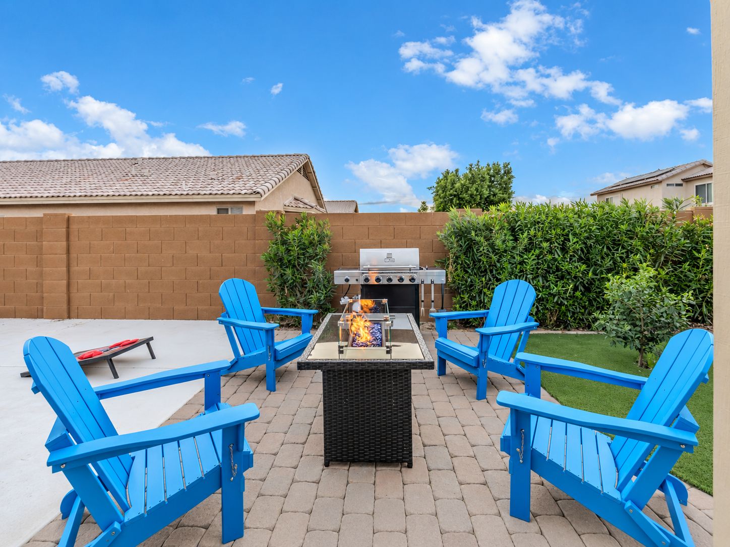 Un patio exterior con una parrilla, cuatro sillas Adirondack azules y un muro de ladrillo.