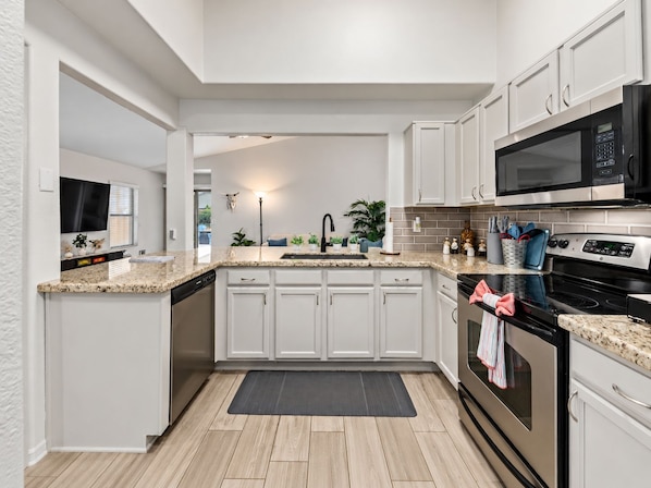 A modern kitchen with white cabinetry, a granite countertop, a black microwave, and a stainless steel oven. - Private Pool Oasis Near Spring Training & Luke AFB (Surprise)