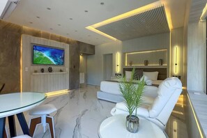 Ein modernes Wohnzimmer mit Flachbildfernseher, einem Glastisch, weißen Sofas und einer Zimmerpflanze.
