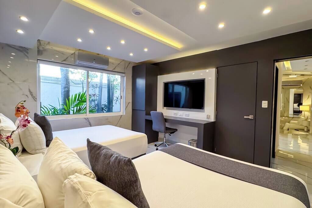 Une chambre d’hôtel moderne, dotée d’un grand lit, d’un téléviseur fixé au mur et d’une fenêtre donnant sur un paysage verdoyant.