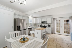 Une cuisine moderne avec des meubles blancs, des appareils en acier inoxydable et un coin repas agrémenté d’une nappe à rayures.