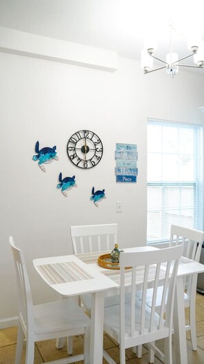 A dining area with a white table and chairs, a wall clock, and decorative turtle figurines. - Historic Hideaway - Downtown/Night of Lights getaway! (St. Augustine)
